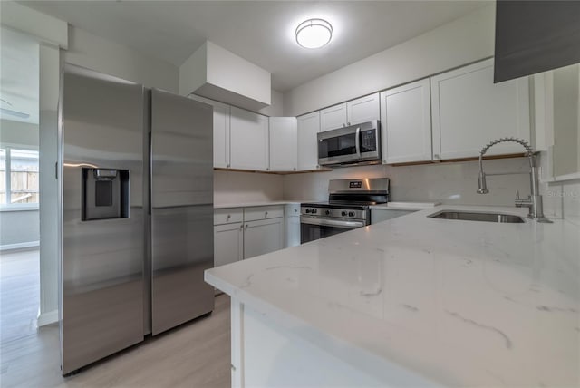 kitchen with white cabinets, appliances with stainless steel finishes, light stone counters, and sink