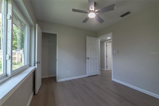 unfurnished bedroom featuring hardwood / wood-style flooring, ceiling fan, a closet, and multiple windows