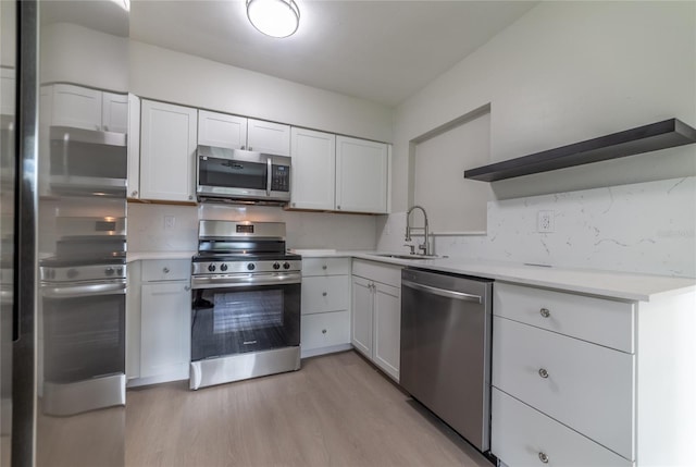 kitchen featuring appliances with stainless steel finishes, light wood-type flooring, tasteful backsplash, sink, and white cabinetry