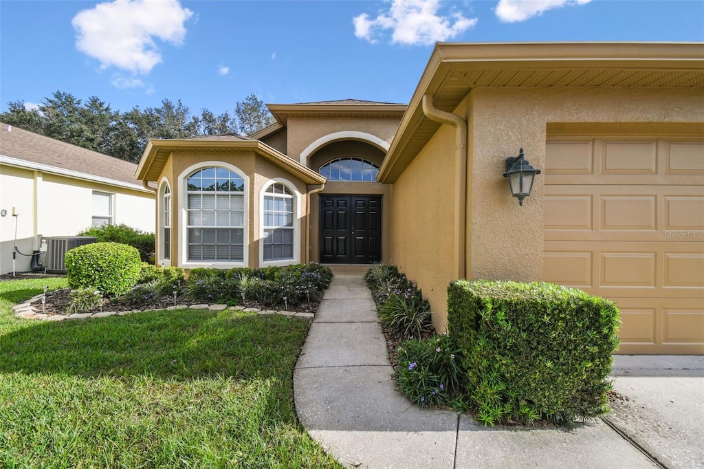 entrance to property featuring a yard, a garage, and central AC unit