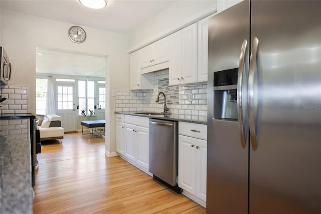 kitchen featuring appliances with stainless steel finishes, sink, light wood-type flooring, white cabinets, and dark stone countertops