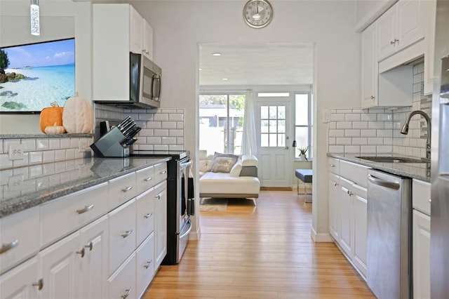 kitchen with dark stone counters, sink, white cabinets, light wood-type flooring, and appliances with stainless steel finishes