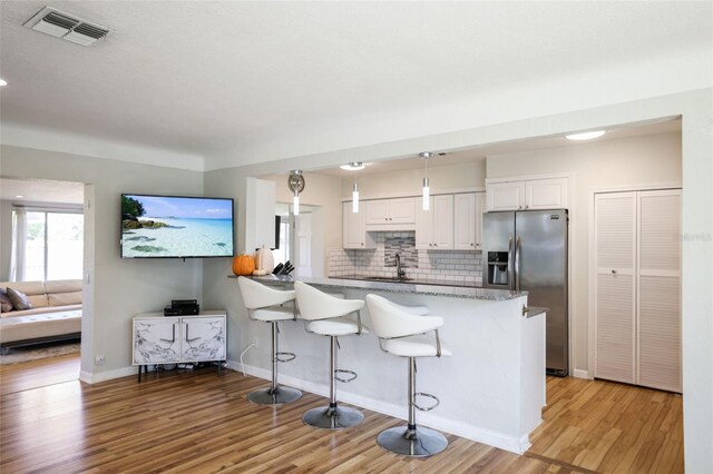 kitchen with a breakfast bar, kitchen peninsula, white cabinetry, stainless steel fridge with ice dispenser, and light hardwood / wood-style flooring