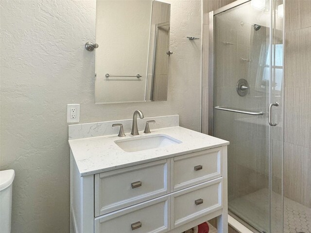 bathroom featuring a shower with door, vanity, and toilet