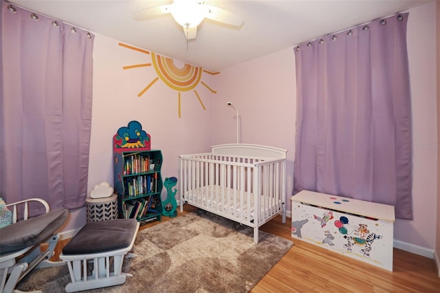 bedroom featuring hardwood / wood-style floors, a nursery area, and ceiling fan