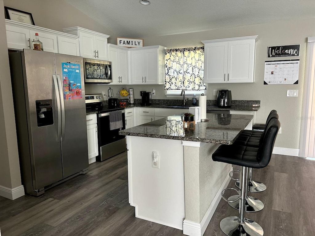 kitchen featuring a kitchen island, stainless steel appliances, sink, white cabinets, and dark hardwood / wood-style flooring