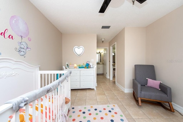 tiled bedroom with a nursery area, ceiling fan, a textured ceiling, and ensuite bath