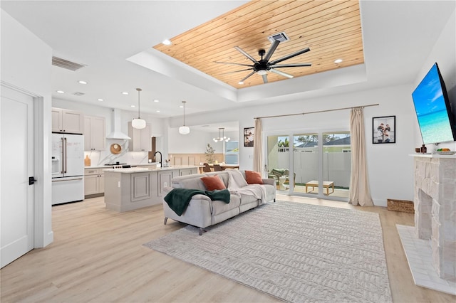 living room with light hardwood / wood-style flooring, wood ceiling, a tray ceiling, and ceiling fan with notable chandelier