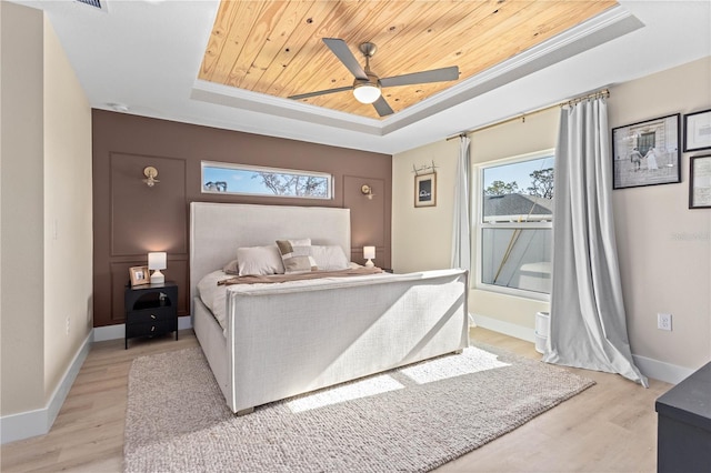 bedroom featuring multiple windows, a tray ceiling, and light wood-type flooring