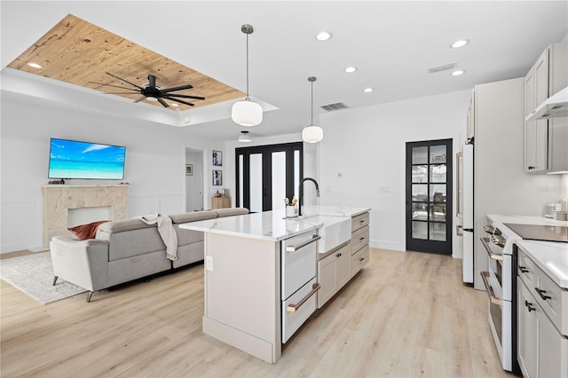 kitchen with a kitchen island with sink, light hardwood / wood-style floors, sink, white cabinetry, and white appliances