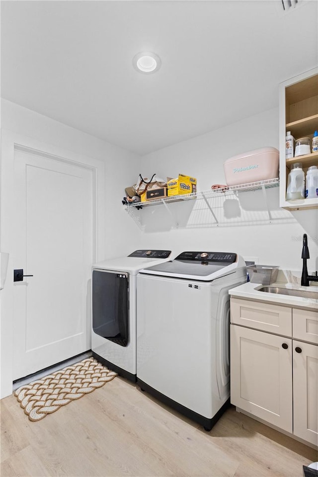 laundry area with sink, light hardwood / wood-style floors, washing machine and dryer, and cabinets