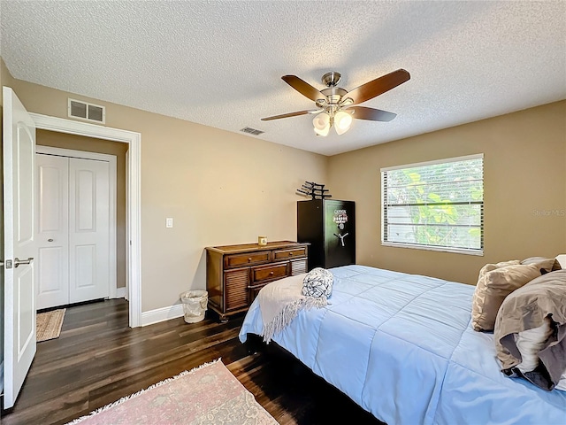 bedroom featuring dark wood-type flooring, ceiling fan, a closet, and a textured ceiling