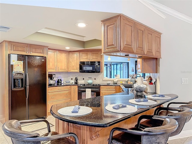 kitchen featuring dark stone countertops, ornamental molding, black appliances, and a breakfast bar area