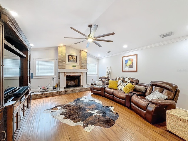 living room featuring lofted ceiling, crown molding, a brick fireplace, light hardwood / wood-style flooring, and ceiling fan