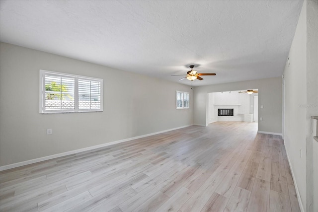 7886 9th Ave S, Saint Petersburg, FL 33707 - unfurnished living room featuring a ceiling fan, light wood-style floors, baseboards, a textured ceiling, and a brick fireplace