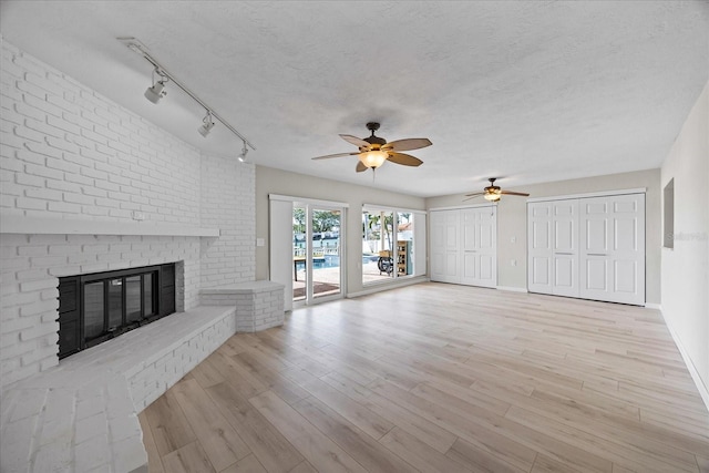 7886 9th Ave S, Saint Petersburg, FL 33707 - unfurnished living room with ceiling fan, a brick fireplace, light wood-style floors, baseboards, and a textured ceiling