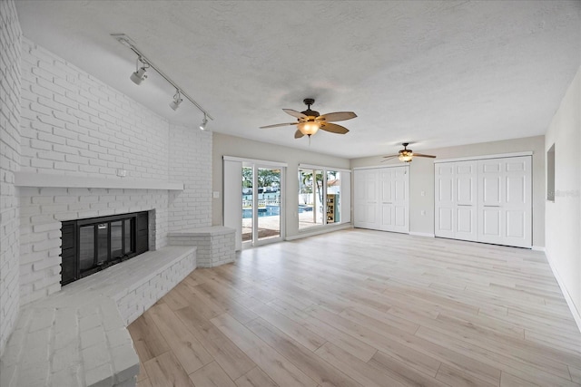 7886 9th Ave S, Saint Petersburg, FL 33707 - unfurnished living room featuring ceiling fan, a fireplace, light wood finished floors, rail lighting, and baseboards