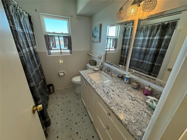 7886 9th Ave S, Saint Petersburg, FL 33707 - bathroom featuring tile walls, vanity, toilet, a wainscoted wall, and a shower with curtain