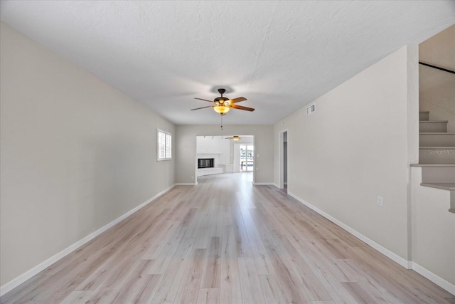 7886 9th Ave S, Saint Petersburg, FL 33707 - unfurnished living room with a ceiling fan, light wood-style flooring, a fireplace, baseboards, and a textured ceiling