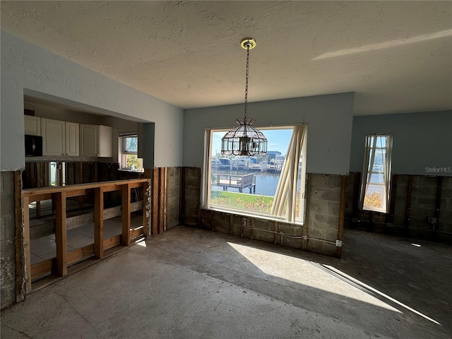 dining room with a chandelier, a healthy amount of sunlight, a water view, and a textured ceiling