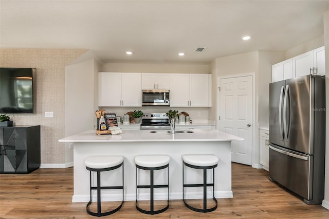 kitchen with a breakfast bar, white cabinetry, light hardwood / wood-style floors, and stainless steel appliances