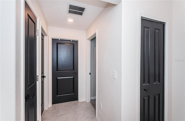 corridor featuring baseboards, visible vents, and light tile patterned floors