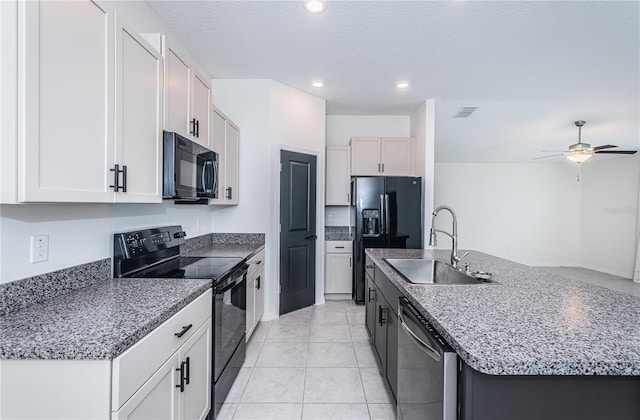 kitchen featuring black appliances, sink, white cabinets, light tile patterned floors, and a center island with sink