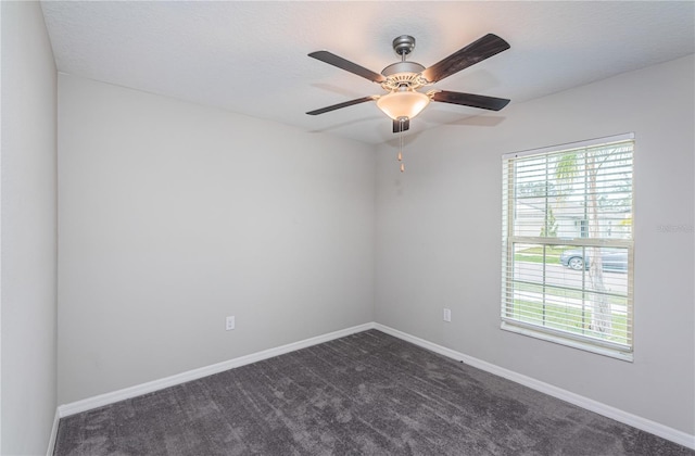 spare room featuring a ceiling fan, dark carpet, a wealth of natural light, and baseboards