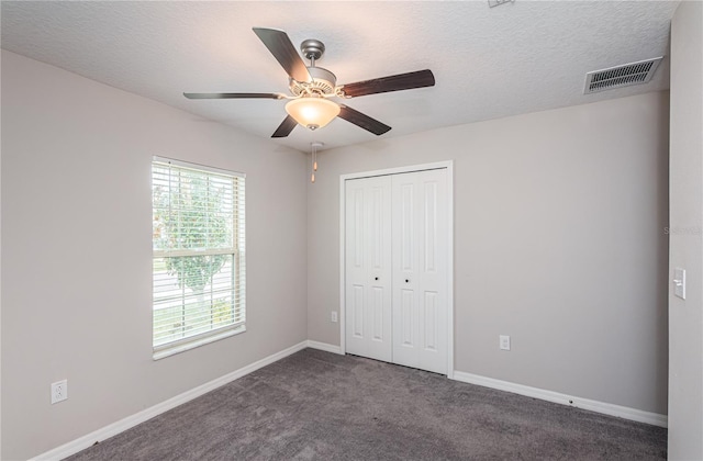 unfurnished bedroom with dark colored carpet, a textured ceiling, a closet, and ceiling fan