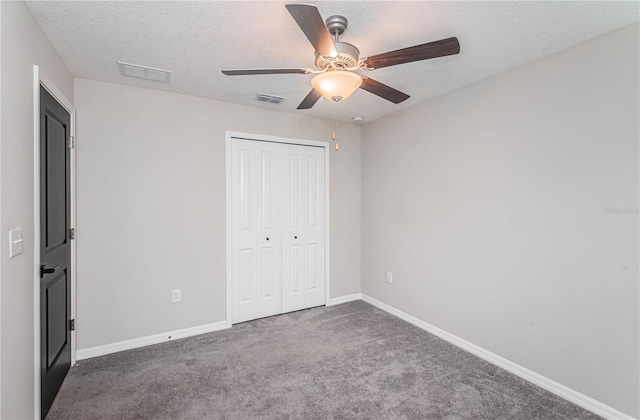 unfurnished bedroom with dark colored carpet, a textured ceiling, a closet, and ceiling fan