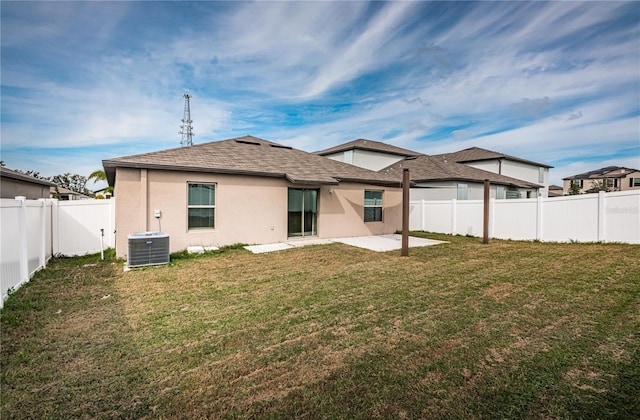 rear view of property with a patio area, a yard, a fenced backyard, central AC, and stucco siding