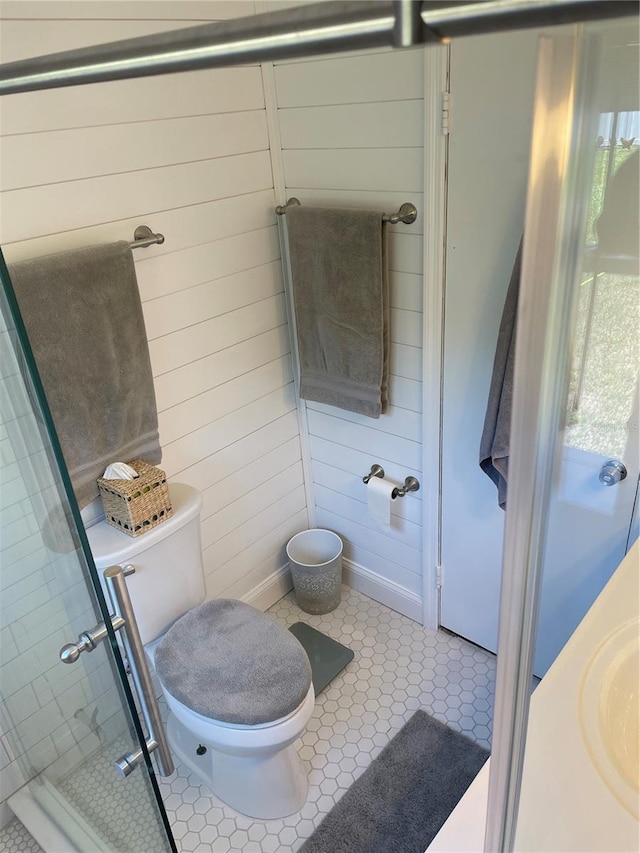 bathroom with tile patterned flooring, toilet, an enclosed shower, and wood walls