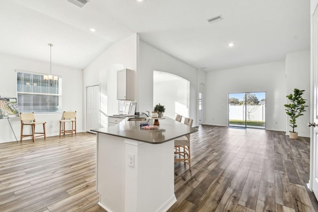 kitchen with lofted ceiling, sink, decorative light fixtures, light wood-type flooring, and kitchen peninsula