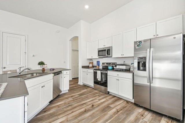 kitchen with appliances with stainless steel finishes, sink, white cabinets, and light hardwood / wood-style flooring