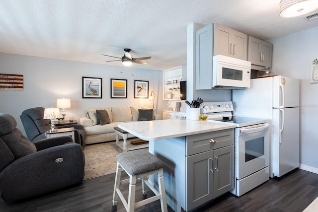 kitchen with a kitchen breakfast bar, dark hardwood / wood-style flooring, gray cabinetry, and white appliances