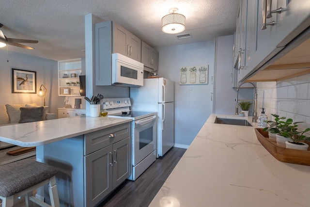 kitchen featuring white appliances, a kitchen bar, a textured ceiling, dark hardwood / wood-style flooring, and decorative backsplash