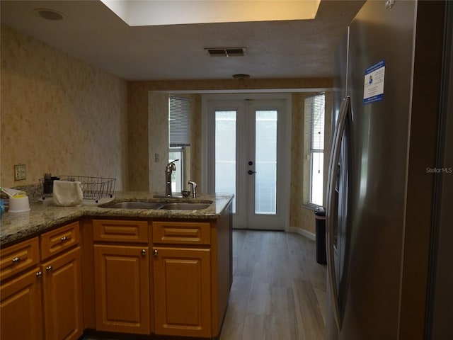 kitchen with french doors, kitchen peninsula, stainless steel fridge, sink, and light hardwood / wood-style floors