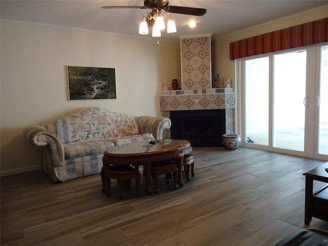 living room featuring ornamental molding, a tiled fireplace, wood-type flooring, and ceiling fan