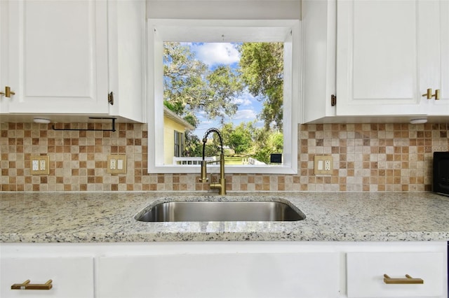 kitchen with white cabinetry, light stone counters, tasteful backsplash, and sink