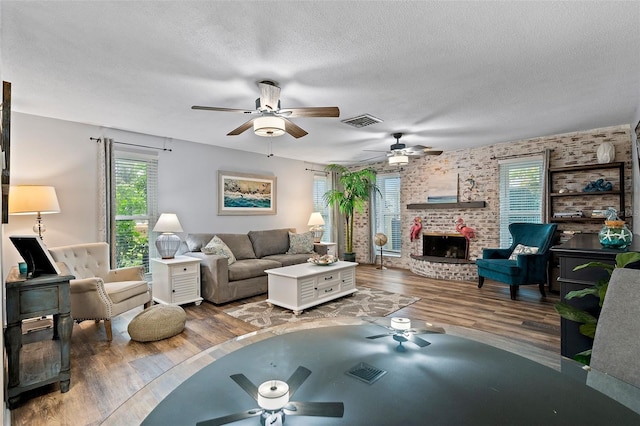 living room with a textured ceiling, a brick fireplace, hardwood / wood-style flooring, and ceiling fan