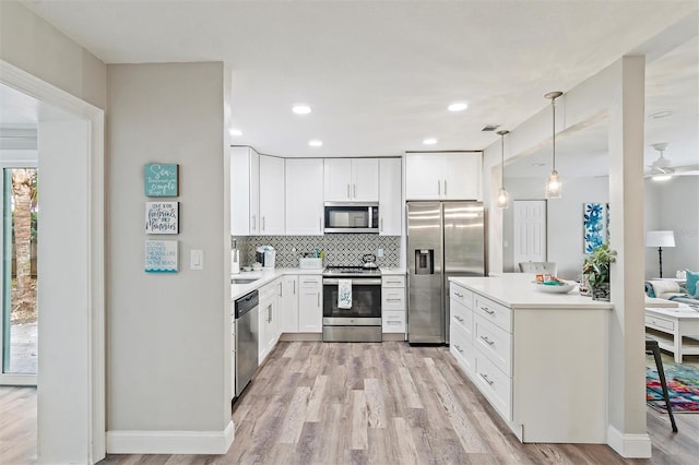 kitchen featuring appliances with stainless steel finishes, white cabinets, hanging light fixtures, and light wood-type flooring