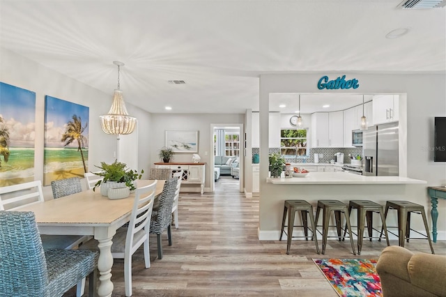 kitchen featuring backsplash, kitchen peninsula, white cabinetry, stainless steel appliances, and light hardwood / wood-style flooring