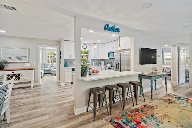 kitchen with appliances with stainless steel finishes, kitchen peninsula, white cabinetry, and light wood-type flooring