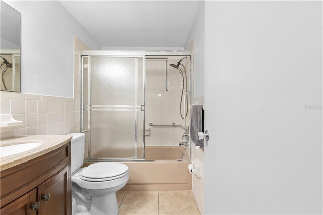 full bathroom with tile patterned floors, toilet, vanity, tile walls, and enclosed tub / shower combo