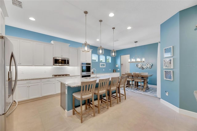 kitchen featuring stainless steel appliances, visible vents, white cabinets, hanging light fixtures, and an island with sink