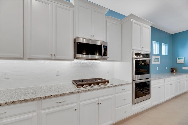 kitchen with light stone counters, decorative backsplash, white cabinetry, and stainless steel appliances