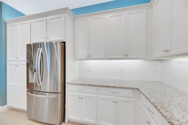 kitchen featuring stainless steel refrigerator with ice dispenser, white cabinets, light stone countertops, and tasteful backsplash