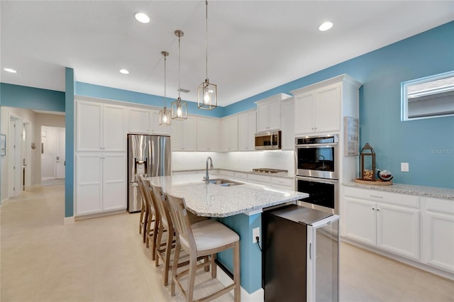 kitchen with sink, white cabinetry, stainless steel appliances, pendant lighting, and a kitchen island with sink