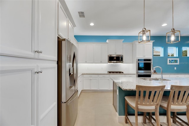 kitchen with a breakfast bar area, sink, pendant lighting, appliances with stainless steel finishes, and light stone counters