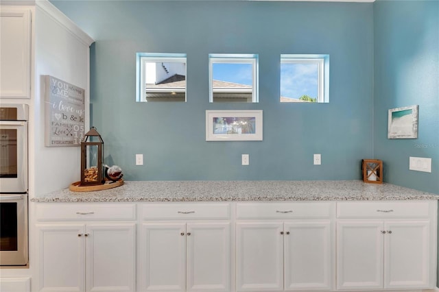 kitchen featuring light stone counters, double oven, and white cabinets